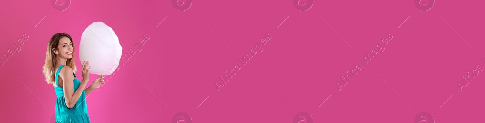 Image of Young woman with sweet cotton candy on bright pink background, space for text. Banner design