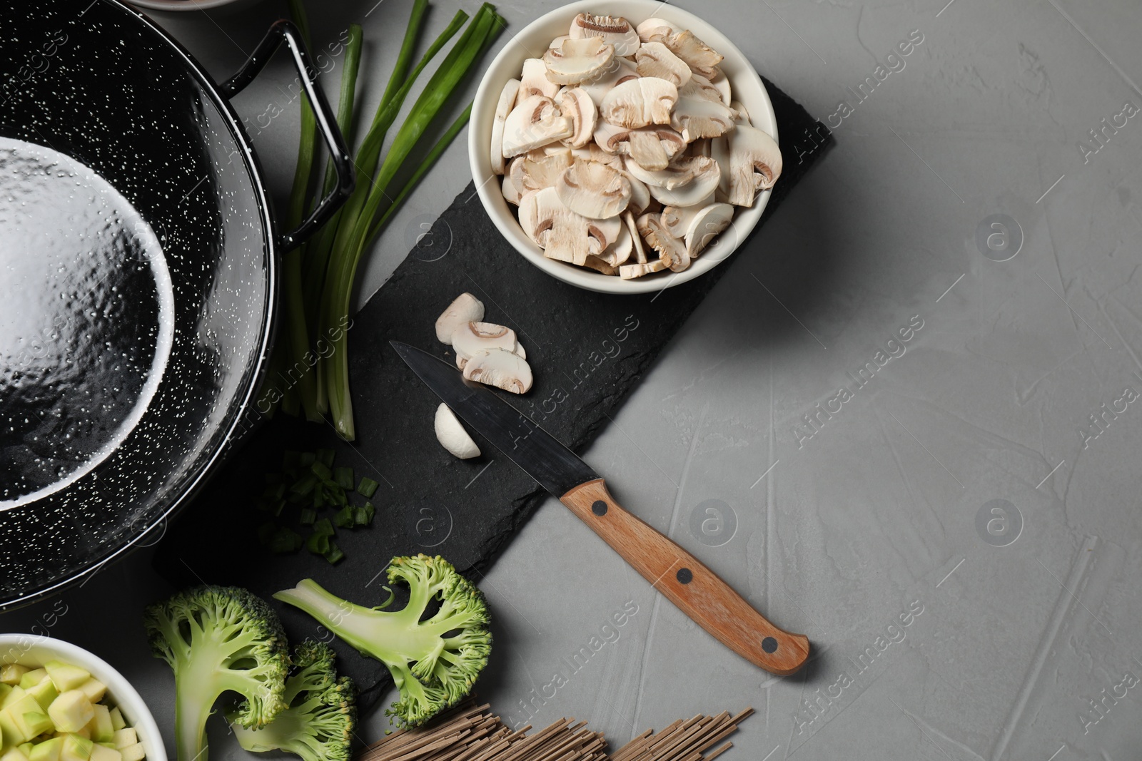 Photo of Wok pan, mushrooms and other products on light grey table, flat lay. Space for text