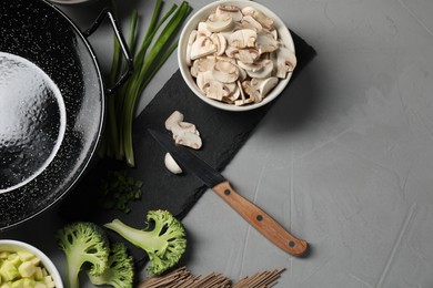 Wok pan, mushrooms and other products on light grey table, flat lay. Space for text