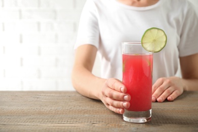 Young woman with glass of tasty refreshing drink at wooden table, closeup