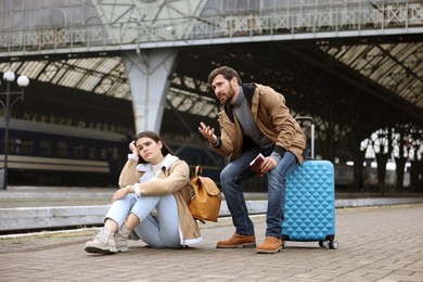 Being late. Worried couple with suitcase waiting at train station