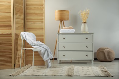 Comfortable chair, chest of drawers and floor lamp in room. Interior design