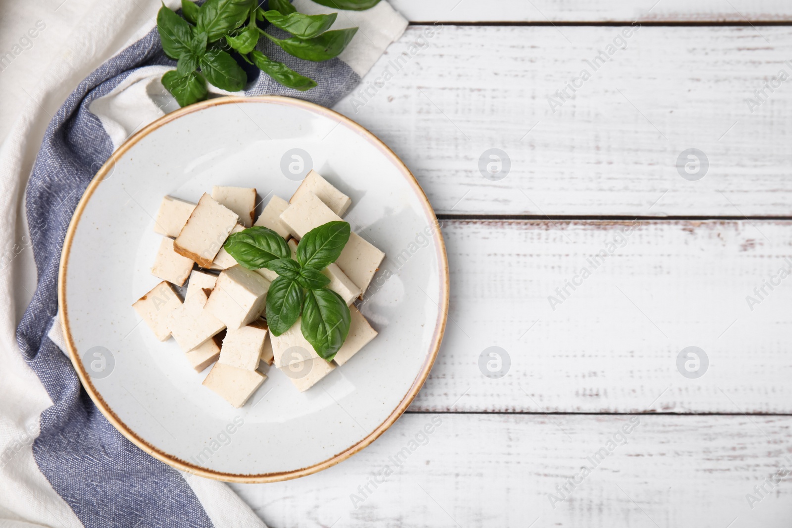 Photo of Plate with delicious smoked tofu and basil on white wooden table, top view. Space for text