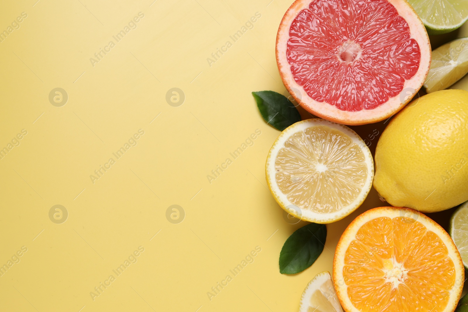 Photo of Different cut and whole citrus fruits on yellow table, flat lay. Space for text