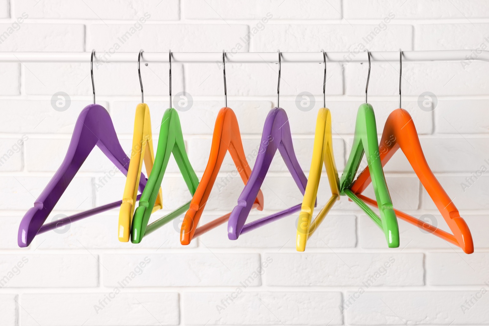 Photo of Colorful clothes hangers on rail near white brick wall