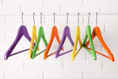 Photo of Colorful clothes hangers on rail near white brick wall