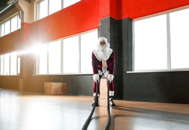 Photo of Young Santa Claus training with ropes in modern gym