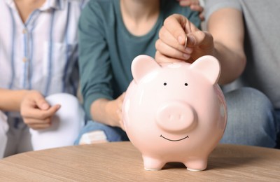 Family with piggy bank at table, closeup of hands