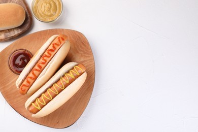 Photo of Tasty hot dogs with ketchup and mustard on white table, flat lay. Space for text