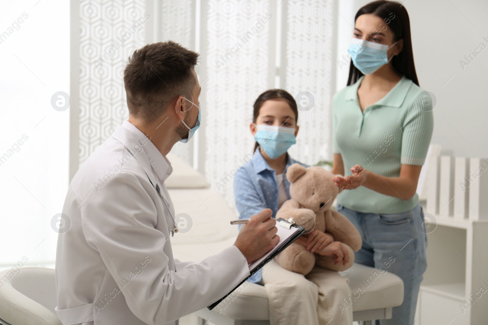 Photo of Mother with daughter visiting pediatrician in hospital. Wearing protective masks