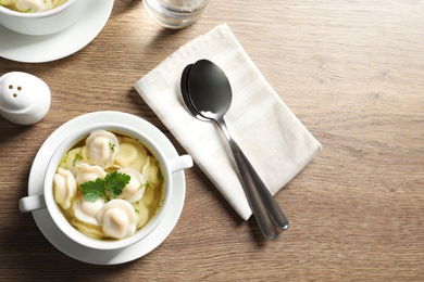 Photo of Bowl on tasty dumplings in broth served on wooden table, flat lay. Space for text