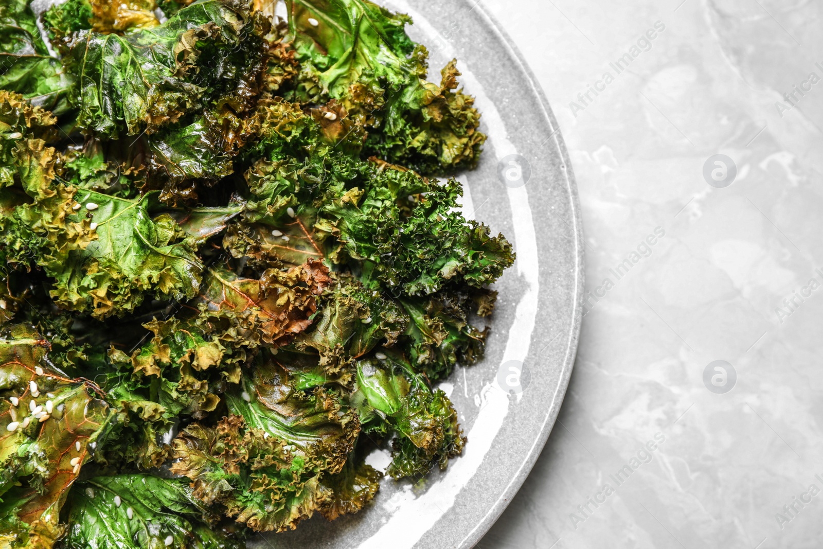 Photo of Tasty baked kale chips on light grey marble table, top view