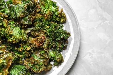 Photo of Tasty baked kale chips on light grey marble table, top view