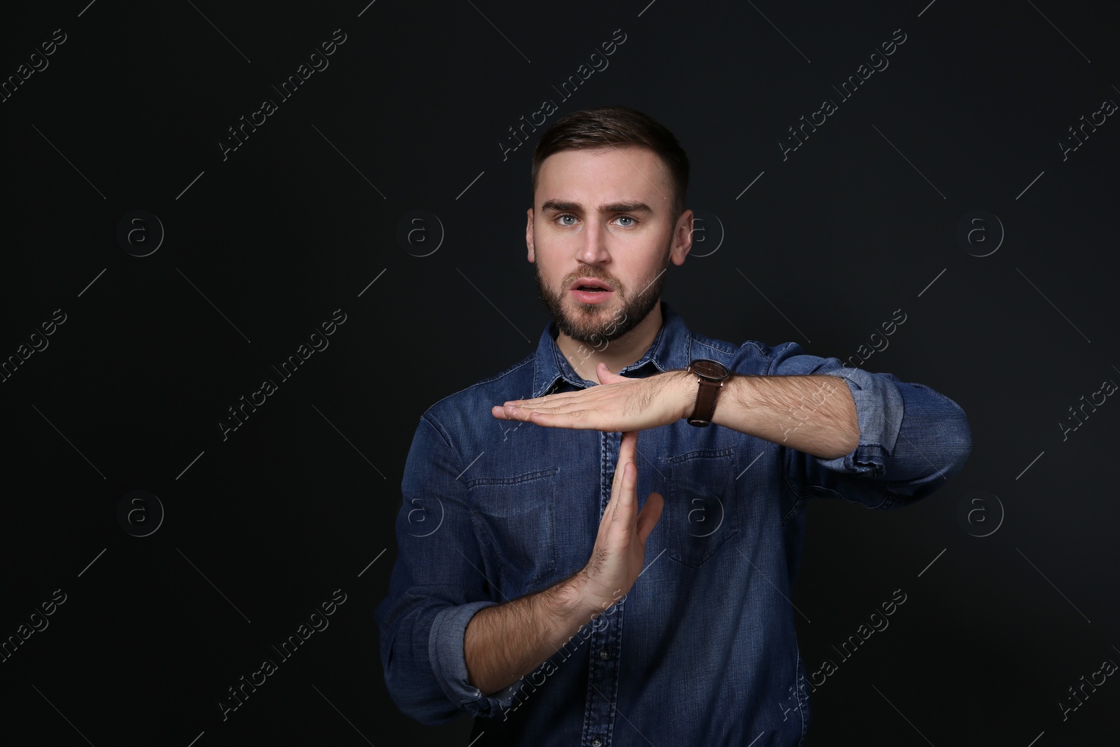 Photo of Man showing TIME OUT gesture in sign language on black background