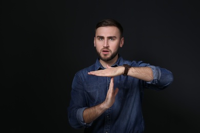 Man showing TIME OUT gesture in sign language on black background
