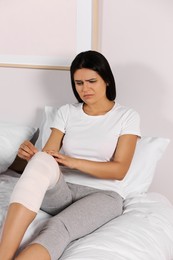 Photo of Young woman with leg wrapped in medical bandage in bedroom