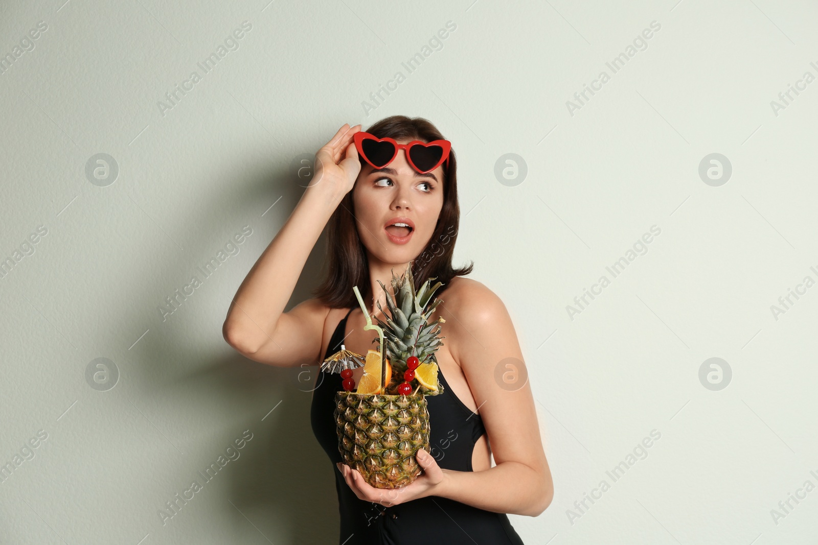 Photo of Beautiful woman in stylish swimsuit holding tropical cocktail on light grey background