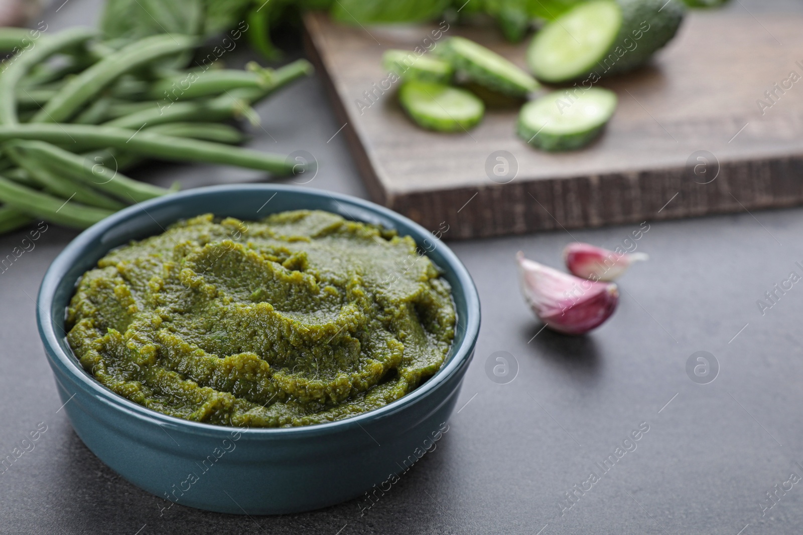 Photo of Bowl with tasty green puree and ingredients on black table, closeup