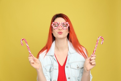 Photo of Young woman with bright dyed hair holding candy canes on yellow background