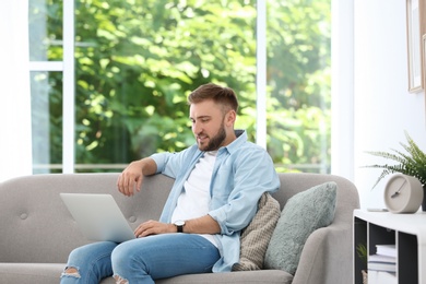 Photo of Young man using laptop while sitting on sofa at home