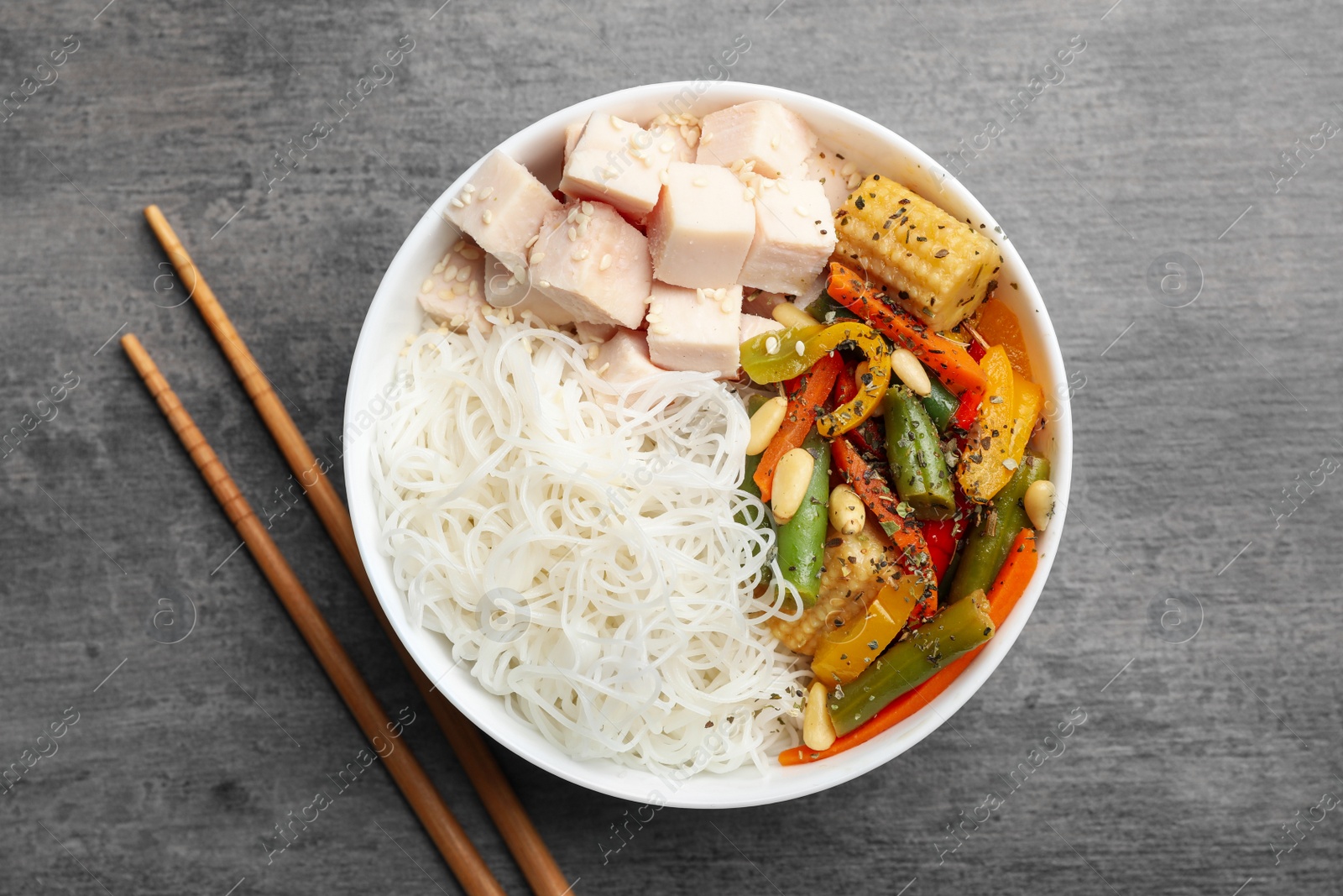 Photo of Tasty cooked rice noodles with chicken and vegetables on grey table, flat lay