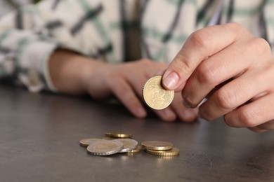 Photo of Poor woman counting coins at grey table, closeup