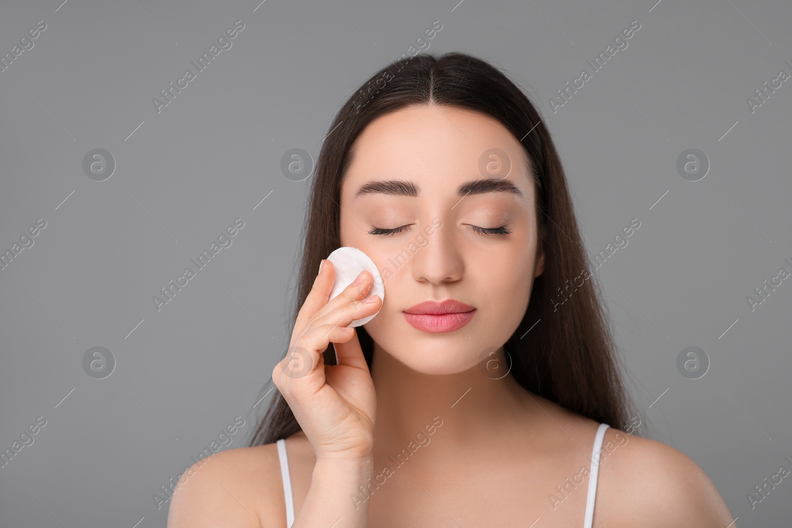 Photo of Beautiful woman removing makeup with cotton pad on gray background