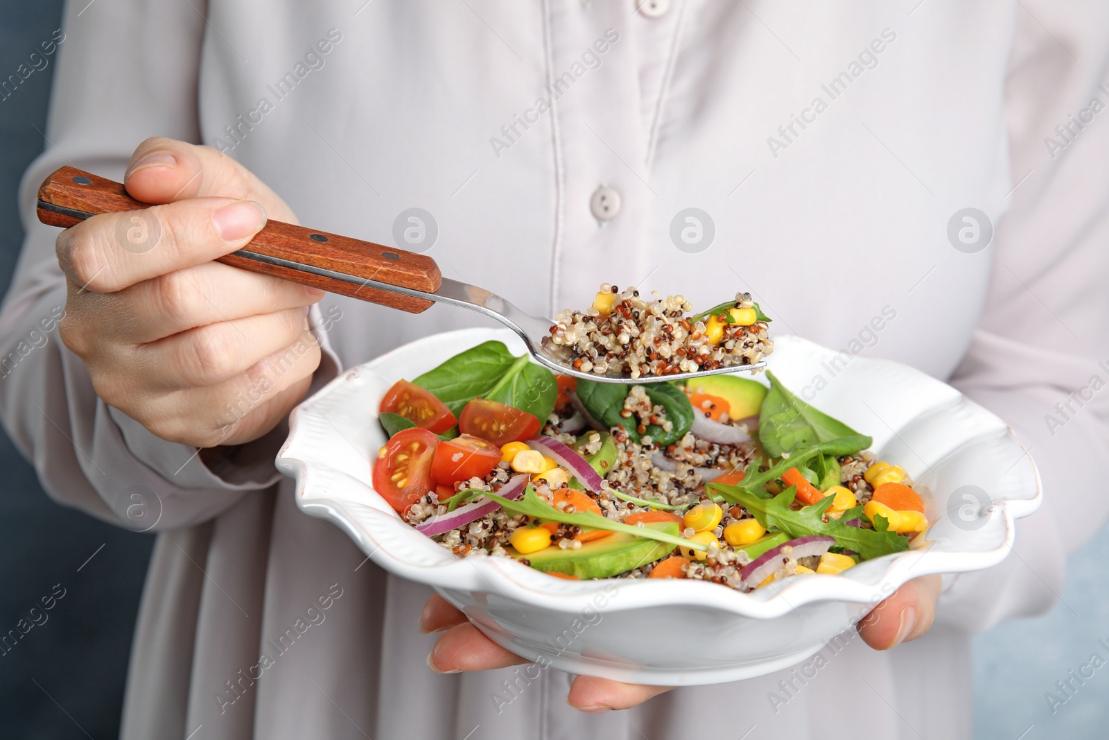 Photo of Woman eating healthy quinoa salad with vegetables from plate, closeup