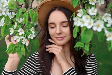 Beautiful woman in hat near blossoming tree on spring day