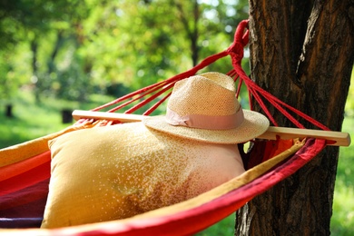 Bright comfortable hammock with pillow and hat hanging in green garden, closeup