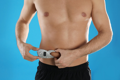 Man measuring body fat layer with digital caliper on light blue background, closeup. Nutritionist's tool