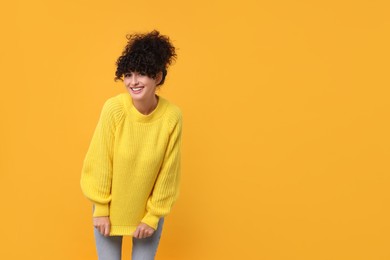 Happy young woman in stylish warm sweater on yellow background, space for text