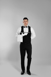 Photo of Handsome butler with tray on light grey background