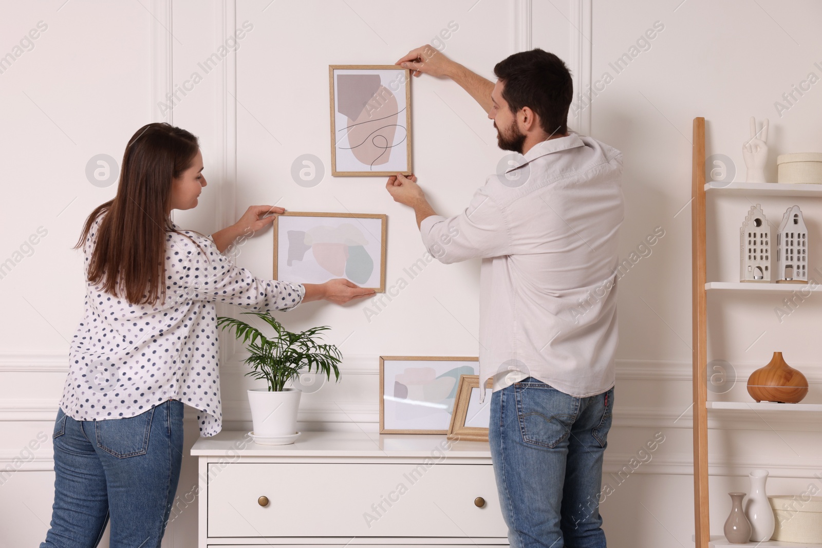 Photo of Man and woman hanging picture frames on white wall at home