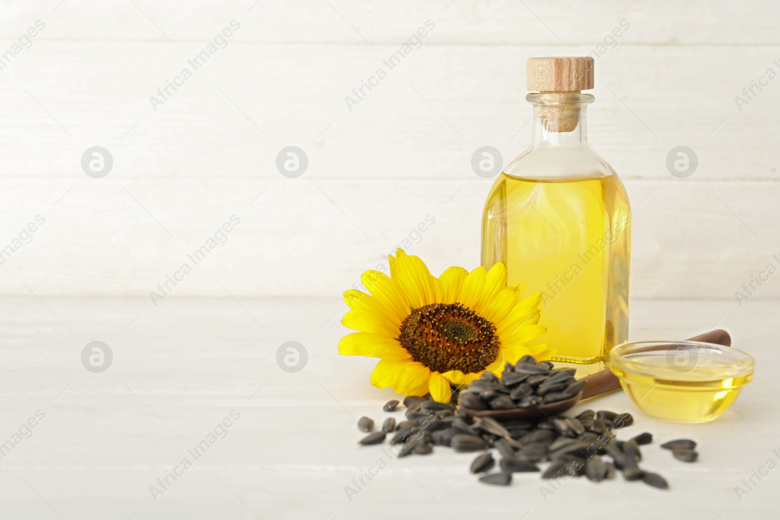 Photo of Sunflower, oil and seeds on white wooden table, space for text