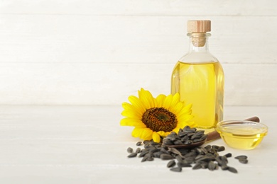 Photo of Sunflower, oil and seeds on white wooden table, space for text