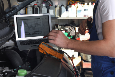 Photo of Mechanic with laptop doing car diagnostic at automobile repair shop, closeup