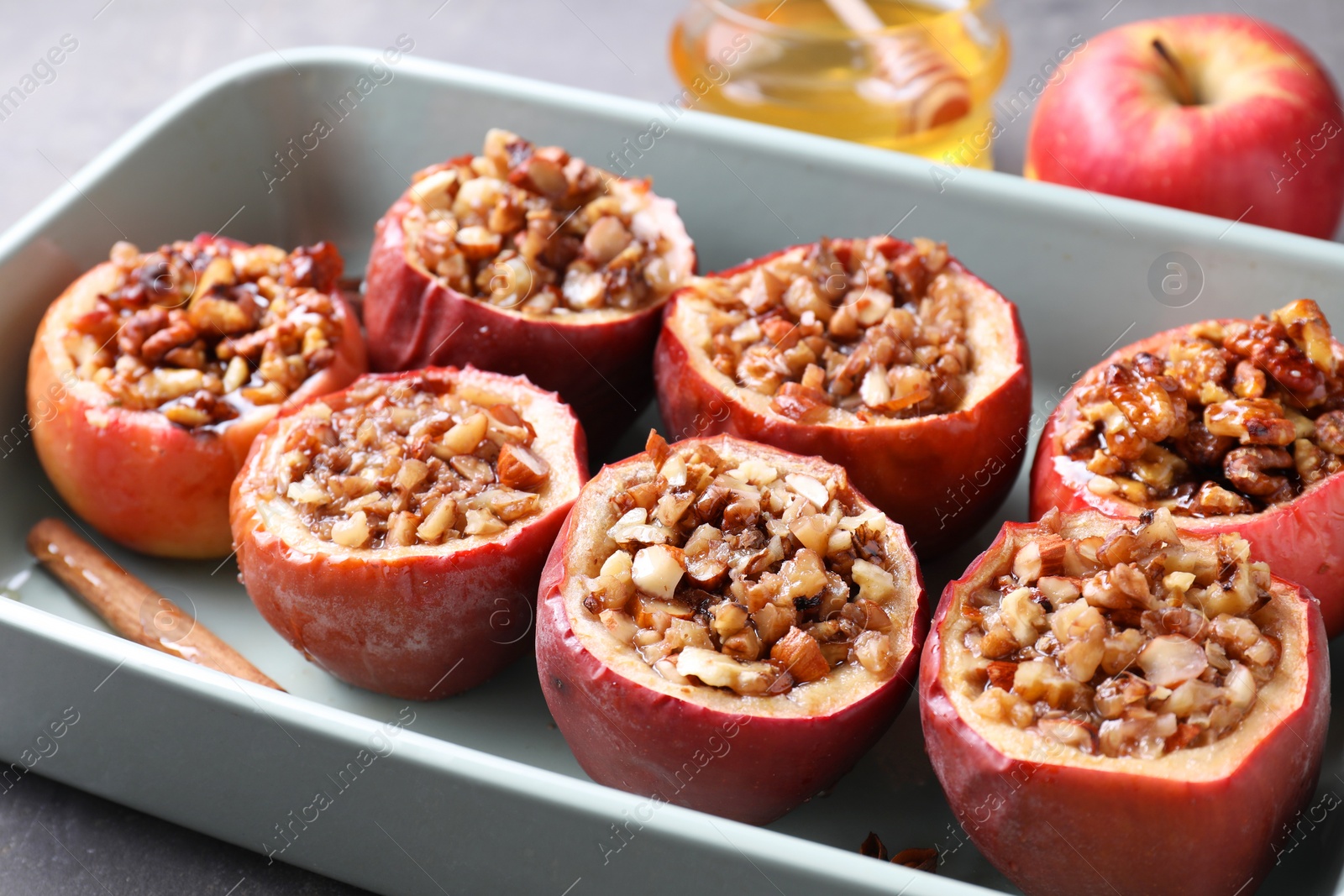 Photo of Tasty baked apples with nuts, honey and cinnamon in dish, closeup