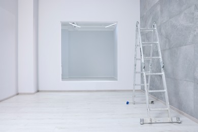 Photo of Empty room with tiled wall, ladder and opening for fake window during repair