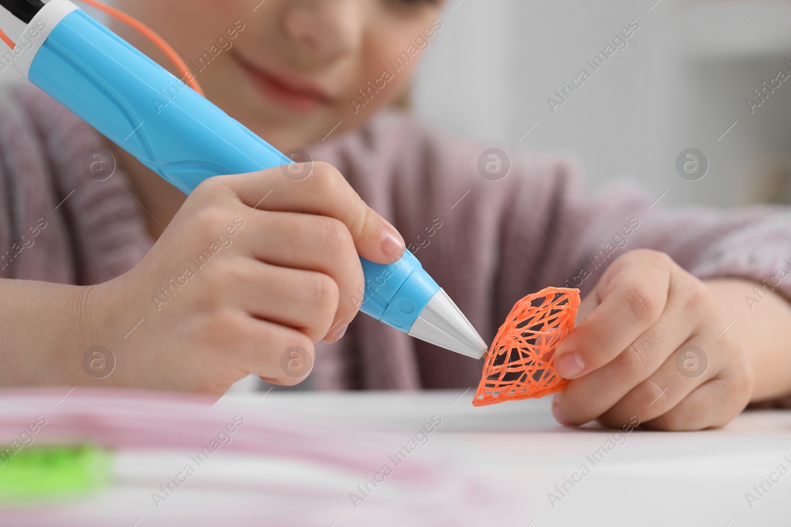 Photo of Girl drawing with stylish 3D pen at white table indoors, closeup