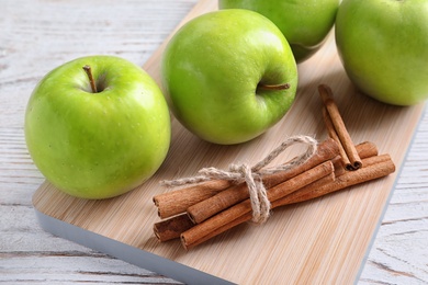 Fresh apples and cinnamon sticks on wooden board