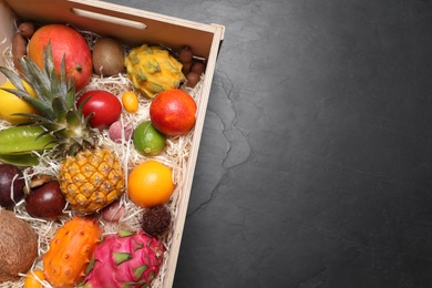 Photo of Crate with different exotic fruits on black table, top view. Space for text