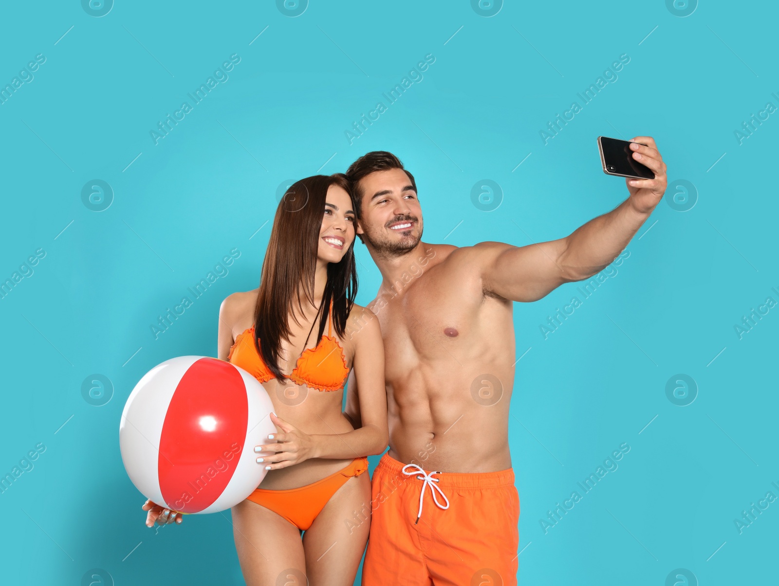 Photo of Young attractive couple in beachwear with ball taking selfie on blue background