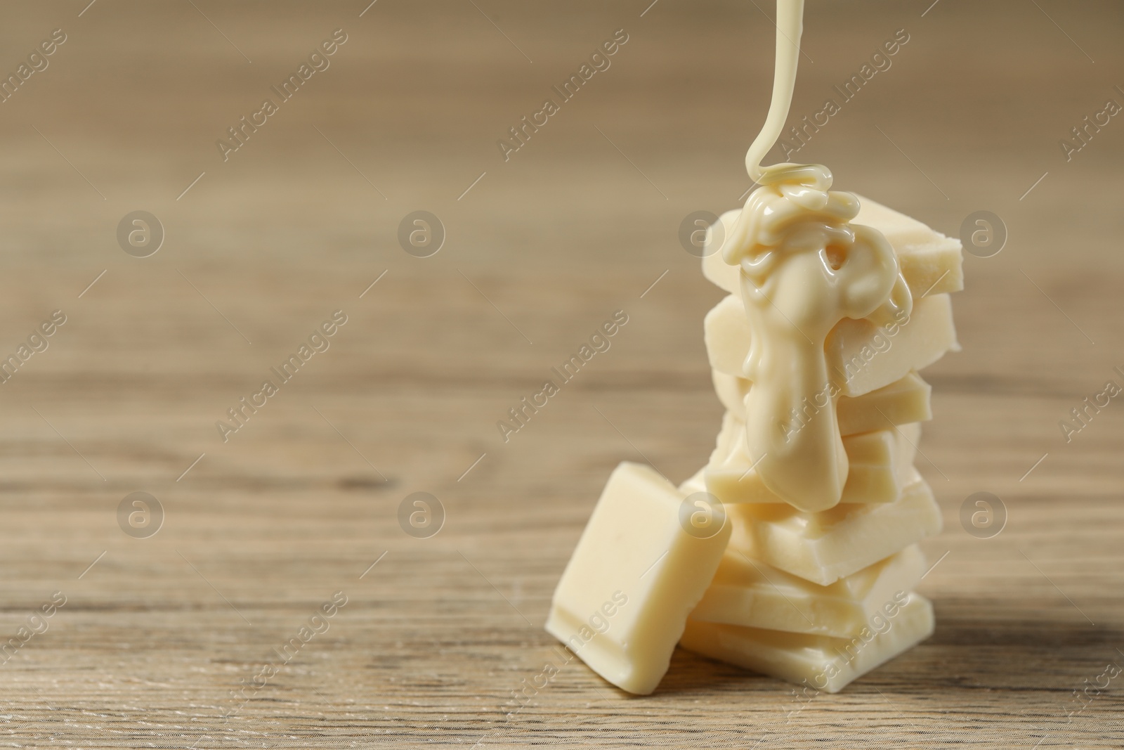 Photo of Pouring tasty white chocolate paste onto pieces on wooden table, closeup. Space for text