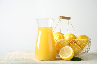 Photo of Basket with ripe lemons and glass jug of fresh juice on table