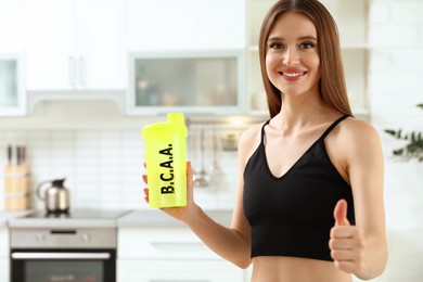 Young woman holding shaker with amino acids (BCAA) drink in kitchen
