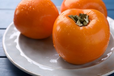 Photo of Delicious ripe persimmons on blue wooden table , closeup