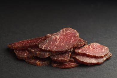 Photo of Pieces of delicious beef jerky on dark table, closeup