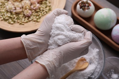 Photo of Woman in gloves holding bath bomb mixture at table, closeup