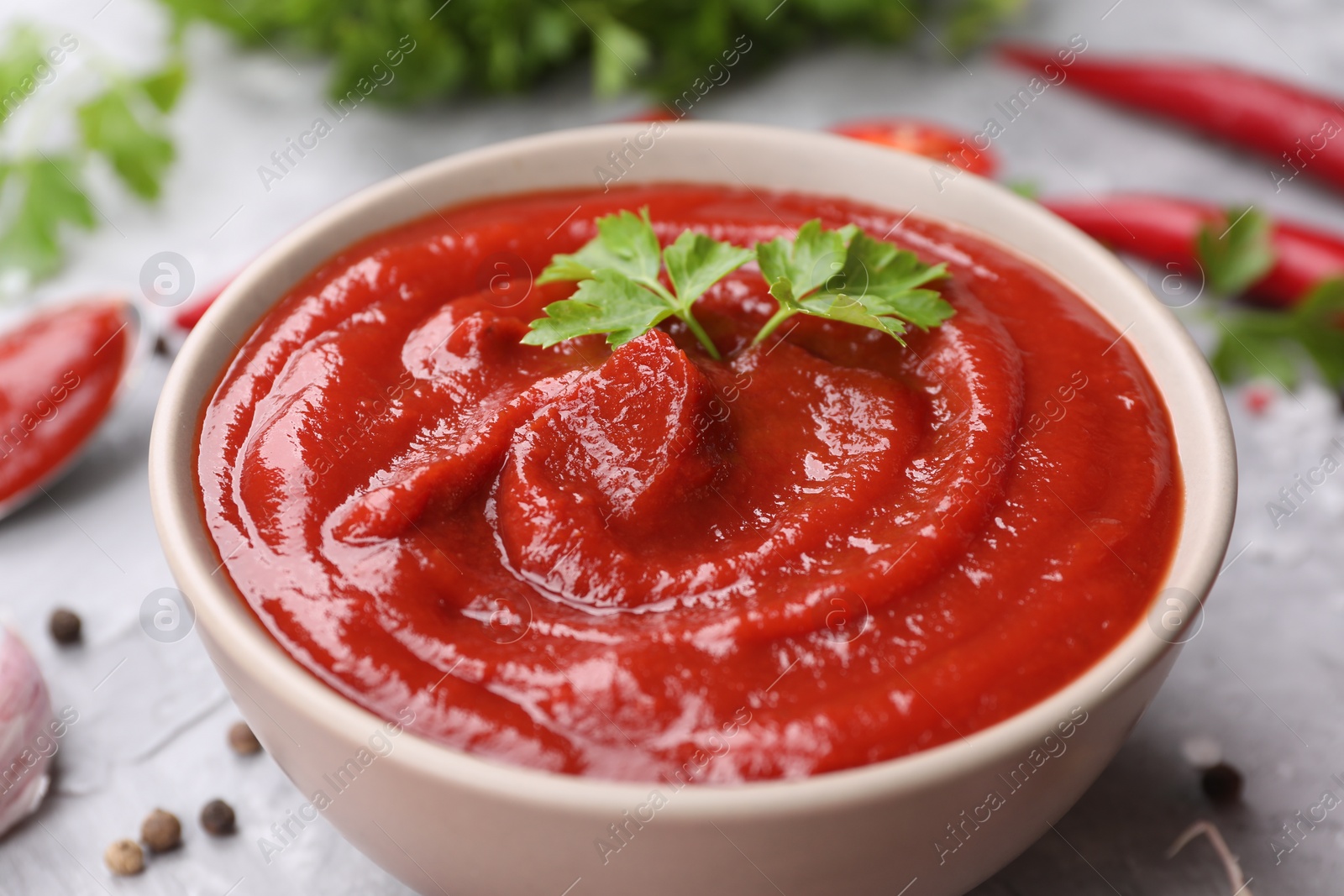 Photo of Organic ketchup and parsley in bowl on grey table, closeup. Tomato sauce